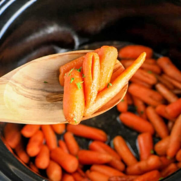 In the cozy embrace of a crockpot, baby carrots simmer to perfection. A wooden spoon lifts the tender morsels, celebrating a simple yet delectable creation.