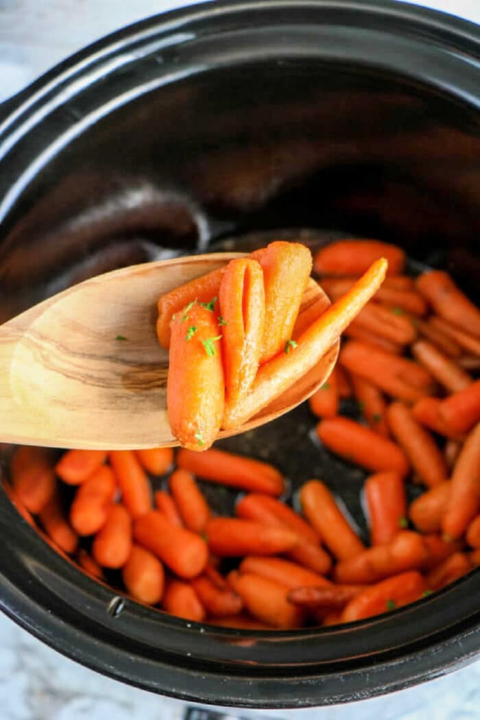 In the cozy embrace of a crockpot, baby carrots simmer to perfection. A wooden spoon lifts the tender morsels, celebrating a simple yet delectable creation.