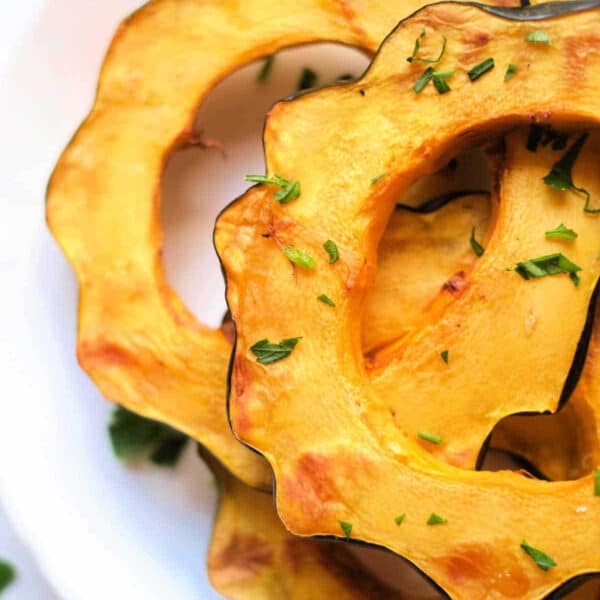 Slices of roasted air fryer acorn squash garnished with chopped herbs on a white plate.