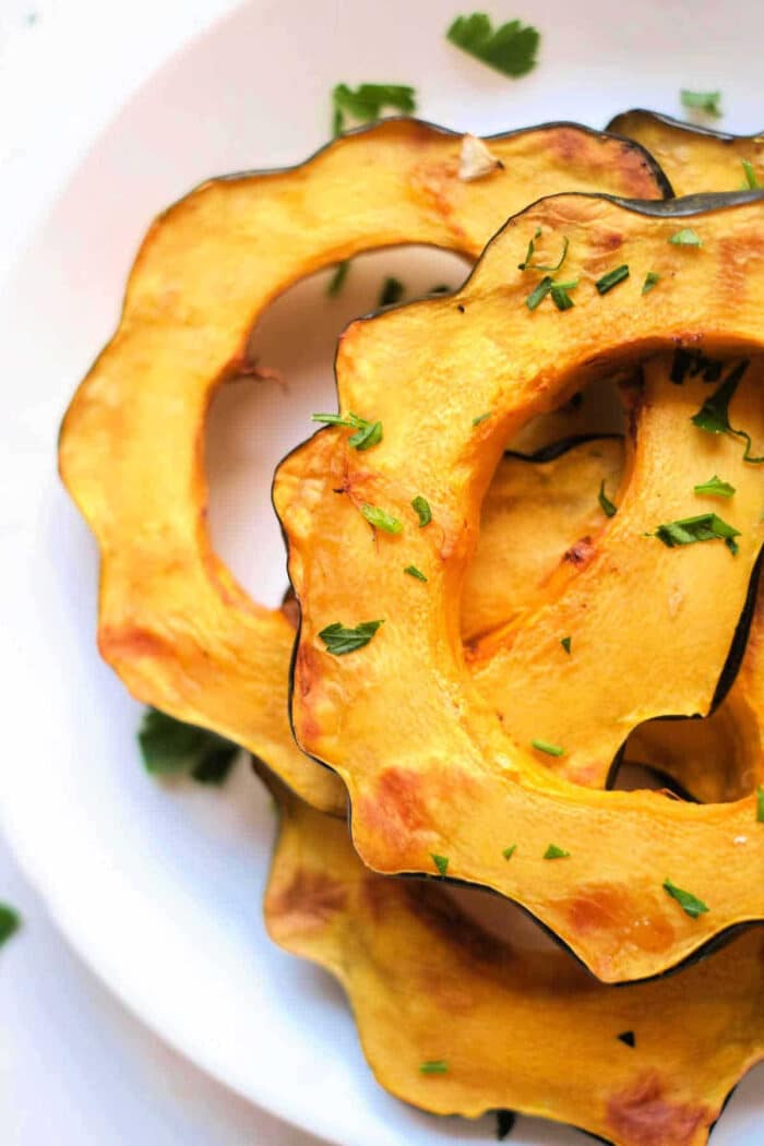 Slices of roasted air fryer acorn squash garnished with chopped herbs on a white plate.