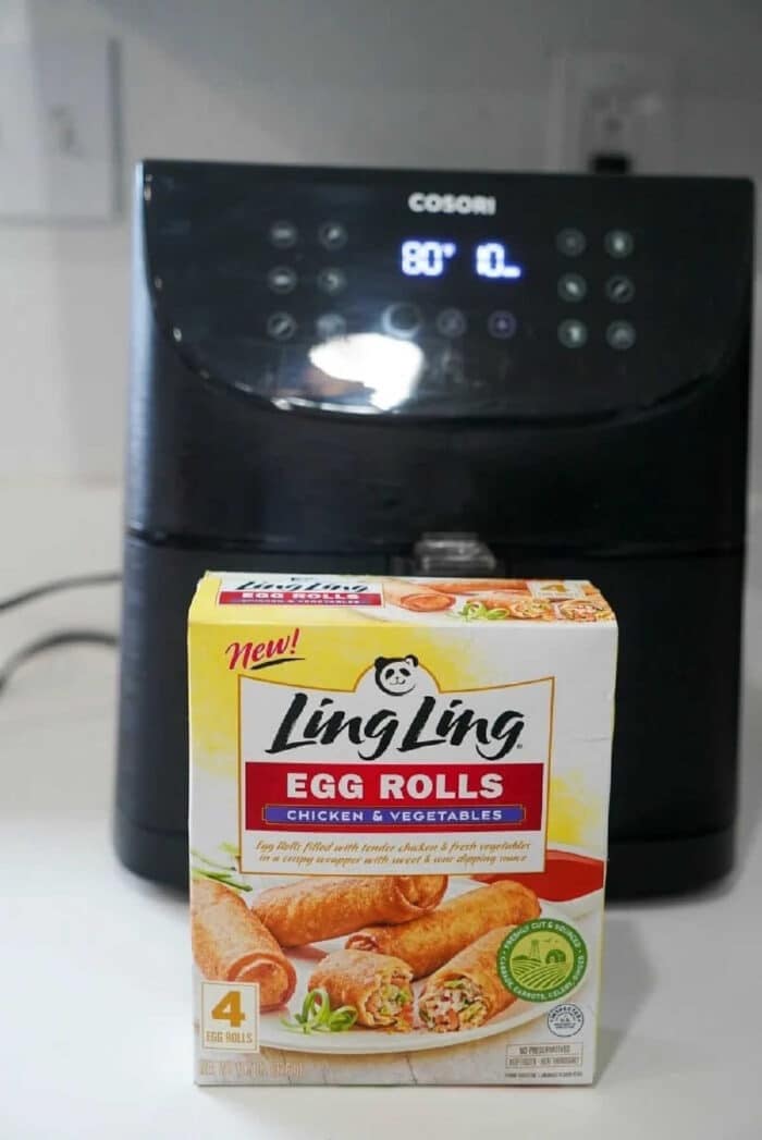 Box of Ling Ling chicken & vegetable egg rolls in front of a Cosori air fryer on a kitchen counter—perfect for making delicious frozen egg rolls in air fryer with ease.