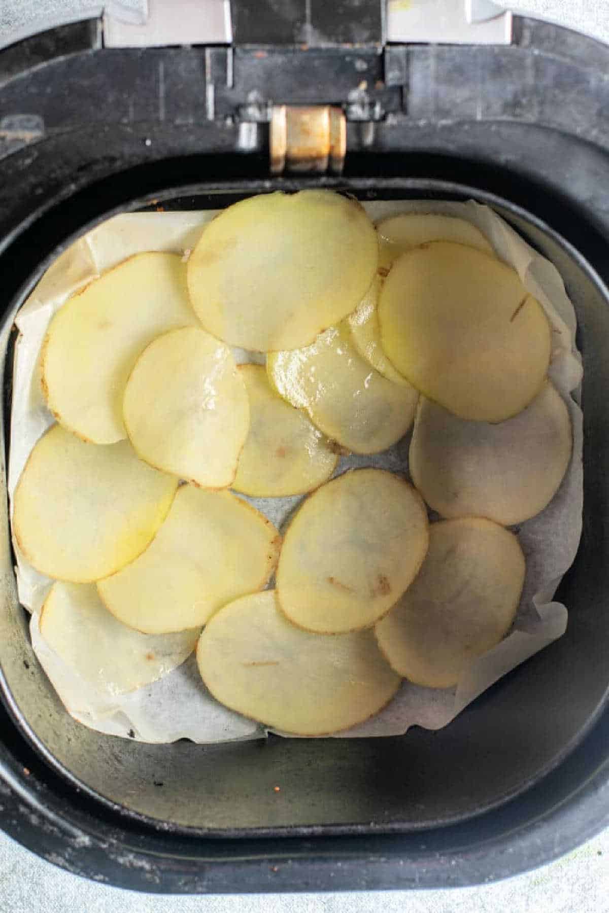 Thin russet potato chips are arranged in a single layer on parchment paper inside an air fryer basket.