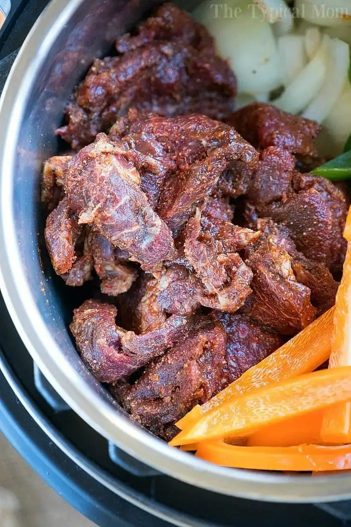 Raw marinated beef pieces in a pot with sliced carrots and onions, infused with the best fajita marinade for an extra burst of flavor.