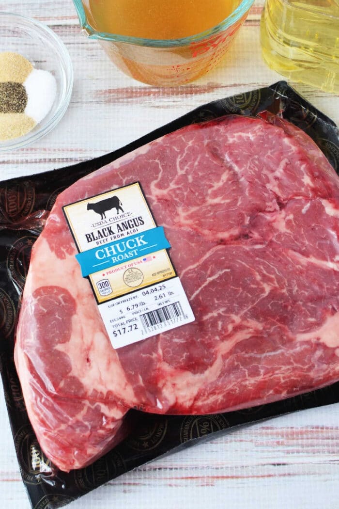 Packaged Black Angus chuck roast on a table with broth, oil, and seasoning bowls nearby—perfect for making savory Mississippi roast in your slow cooker.