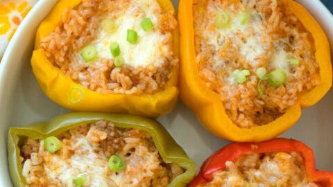 Four easy Instant Pot stuffed peppers, filled with rice, cheese, and scallions, are served in a white bowl for a quick and delicious meal.