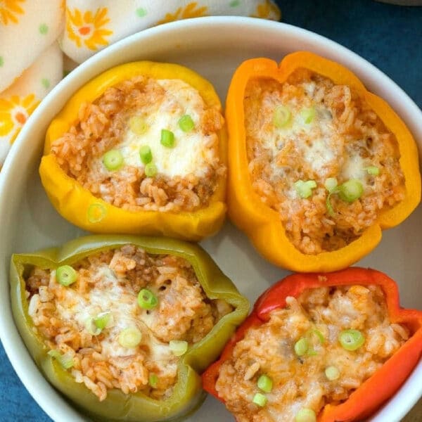 Four easy Instant Pot stuffed peppers, filled with rice, cheese, and scallions, are served in a white bowl for a quick and delicious meal.