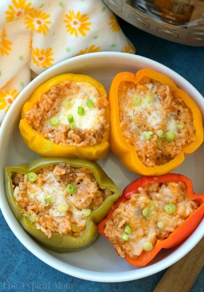Four easy Instant Pot stuffed peppers, filled with rice, cheese, and scallions, are served in a white bowl for a quick and delicious meal.