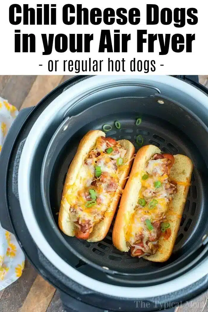 An air fryer contains two chili cheese topped hot dogs on buns. The hot dogs are garnished with chopped green onions and melted cheese. The text above the image reads, "Chili Cheese Dogs in your Air Fryer - or regular air fryer hot dogs -".