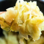 A spoonful of cooked, shredded cabbage is held up close above a pot of more tender Buttered Pressure Cooker Cabbage.