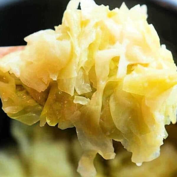 A spoonful of cooked, shredded cabbage is held up close above a pot of more tender Buttered Pressure Cooker Cabbage.