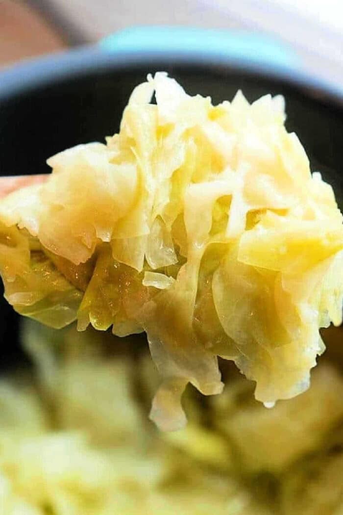 A spoonful of cooked, shredded cabbage is held up close above a pot of more tender Buttered Pressure Cooker Cabbage.