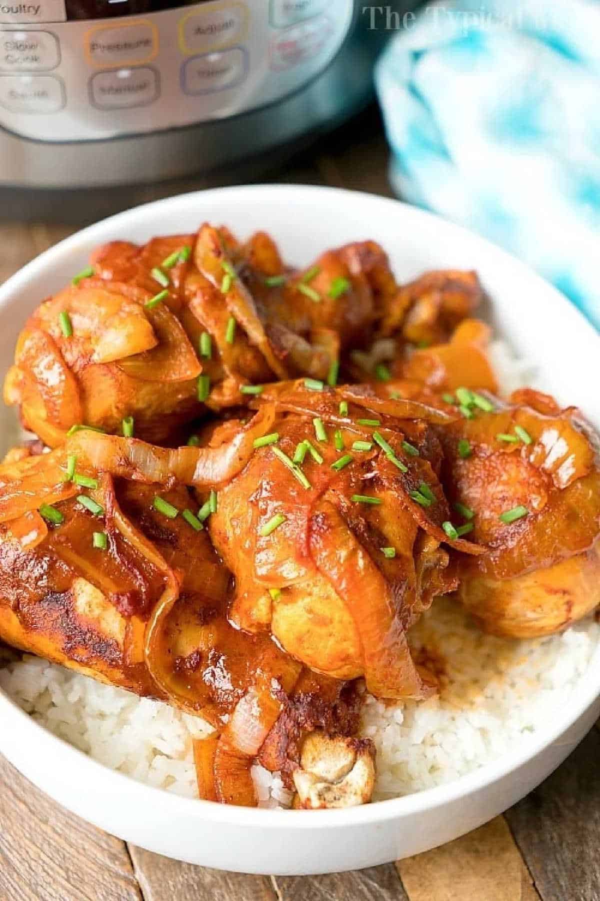 Instant Pot chicken legs are amazing! If you love easy pressure cooker dinners but looking for something your kids will love too chicken drumsticks are simple to make in just 10 minutes. This fall off the bone tender Instant Pot drumstick recipe will be your go to meal for sure! #instantpotrecipes #pressurecooker #chickenlegs #chicken #legs #drumsticks #instantpot #thetypicalmom Instant Pot chicken legs cooked with onions and savory sauce, served over white rice in a bowl, with an Instant Pot in the background.
