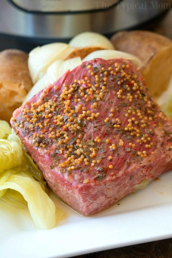 Easy Instant Pot corned beef and cabbage is perfect for St. Patrick's Day or any other day of the year! Moist and flavorful corned beef brisket cooked in your pressure cooker is simple to do with a potato trick I use quite often. If you haven't tried this dinner idea you're in for a treat. #instantpotrecipes #cornedbeefandcabbage #pressurecooker #cornedbeef #brisket #cabbage #crockpotexpress #ninjafoodirecipes A slice of seasoned instant pot corned beef and cabbage, served with potatoes and onions on a white plate.