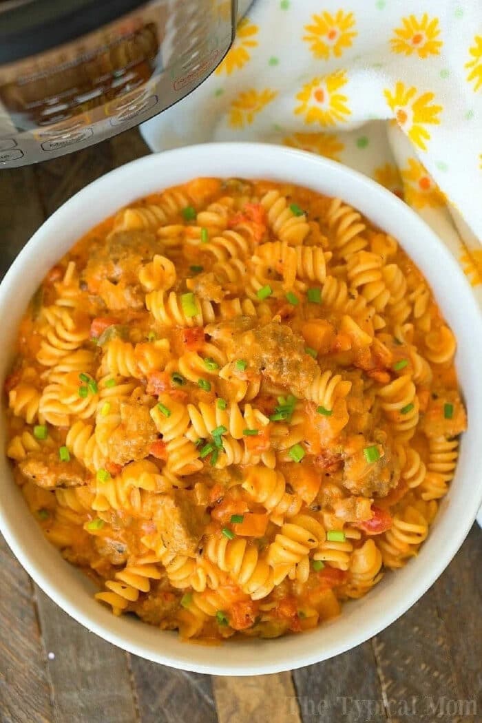Cheesy Instant Pot goulash turned out amazing in my pressure cooker! Creamy goulash with the same flavors you love with two different cheeses within it too. Total comfort food in your pressure cooker that will be your kid's new favorite dinner for sure. #instantpot #pressurecooker #goulash #cheese #cheesy #pasta #casserole #instantpotrecipes #thetypicalmom A bowl of rotini pasta with sausage and creamy tomato sauce, reminiscent of cheesy Instant Pot goulash, garnished with chopped chives.