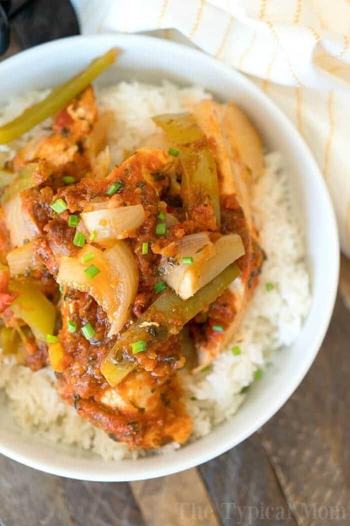A bowl of white rice topped with saucy Instant Pot salsa chicken, bell peppers, onions, and chopped chives.