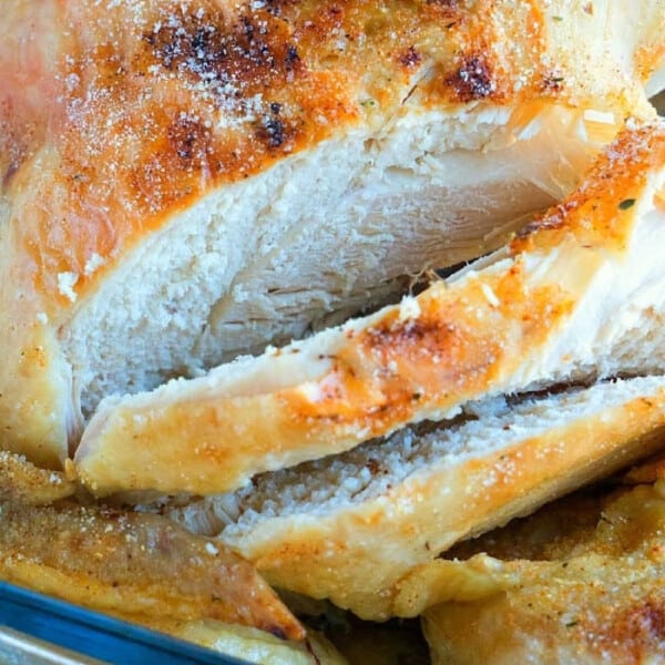 Close-up of a sliced, roasted beer can chicken with golden brown, crispy skin in a glass dish.