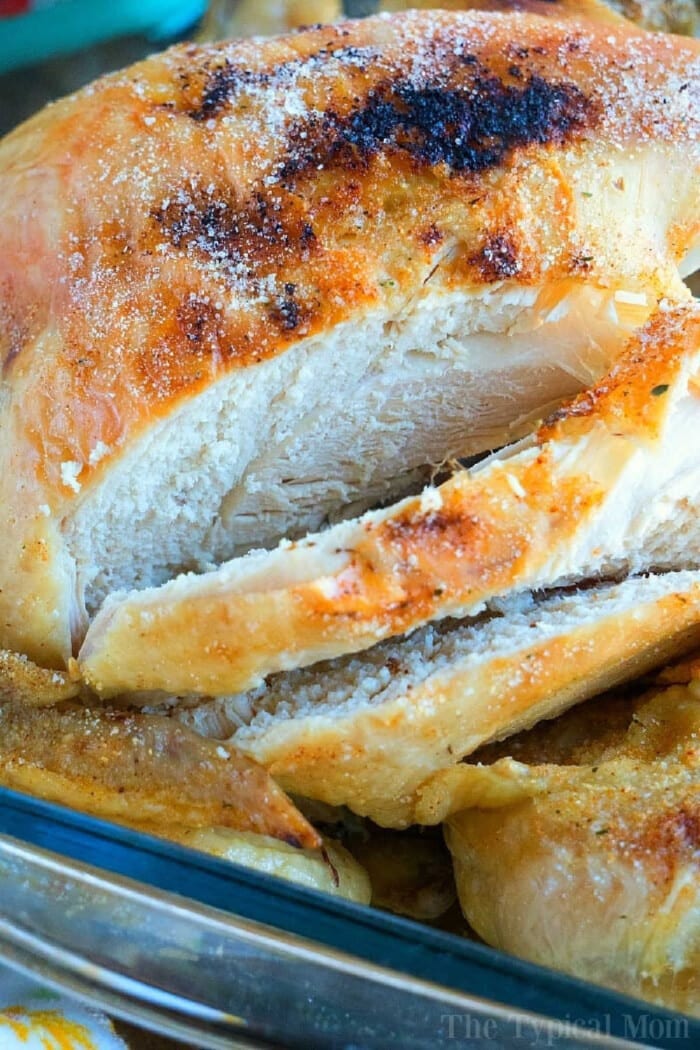 Close-up of a sliced, roasted beer can chicken with golden brown, crispy skin in a glass dish.