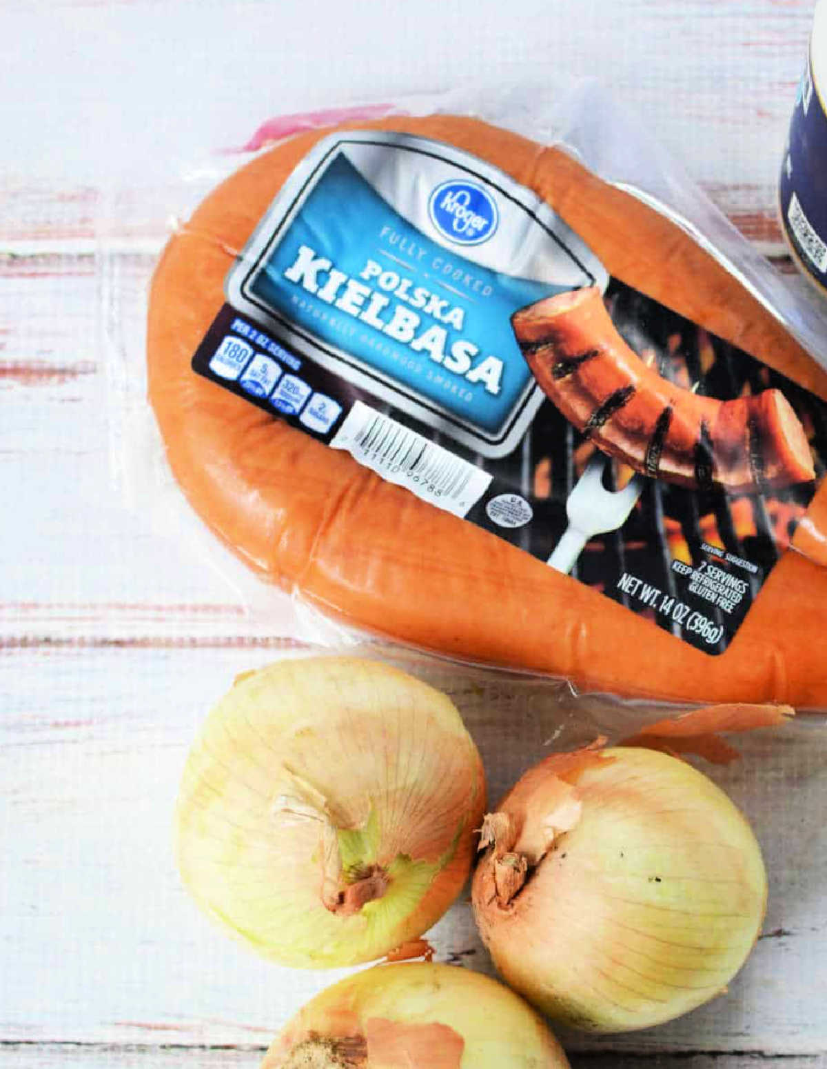 Packaged Polska kielbasa sausage next to three yellow onions on a light wooden surface—perfect ingredients for making instant pot red beans and rice.
