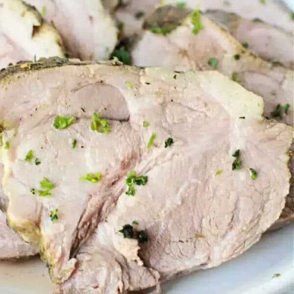 Sliced roast lamb garnished with chopped herbs on a white plate, perfect for fans of simple classics like 3 Ingredient Pork Roast Slow Cooker recipes.
