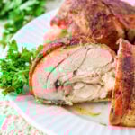Close-up of seasoned, sliced bacon-wrapped chicken thighs on a white plate, garnished with fresh parsley.