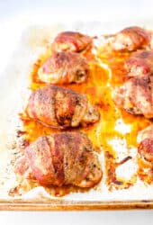 Bacon-wrapped chicken thighs perfectly arranged on a baking sheet, each piece boasting irresistibly crispy edges.