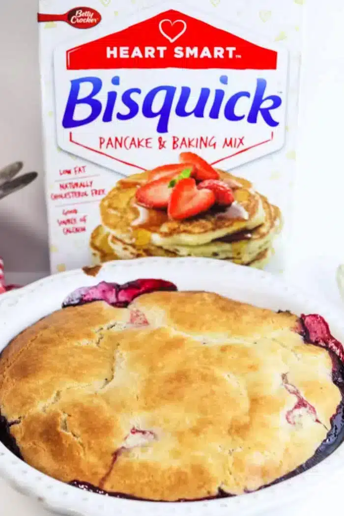 A freshly baked blackberry cobbler sits invitingly in front of a box of Bisquick Heart Smart Pancake & Baking Mix. The golden brown crust reveals juicy fruit beneath, while the box showcases fluffy pancakes topped with strawberries.