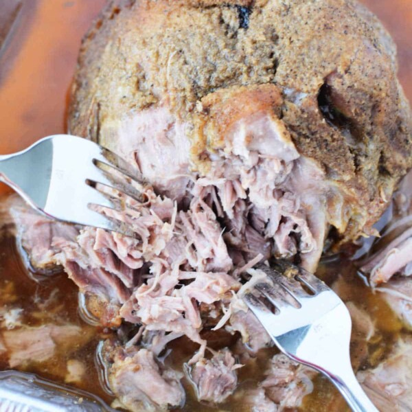 Shredded Boston Butt in a baking pan with two forks pulling the tender roast pork apart.