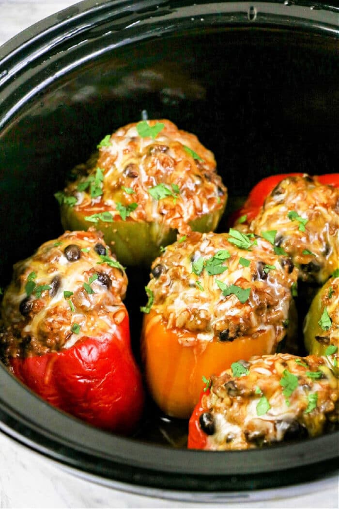 Six crockpot stuffed bell peppers with melted cheese and herbs nestled inside a slow cooker.