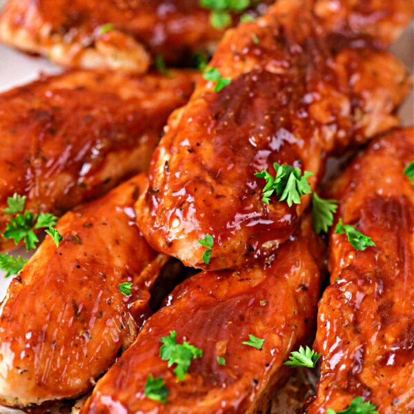 Succulent oven-baked chicken tenders glisten with a savory glaze, elegantly garnished with fresh parsley on a plate.