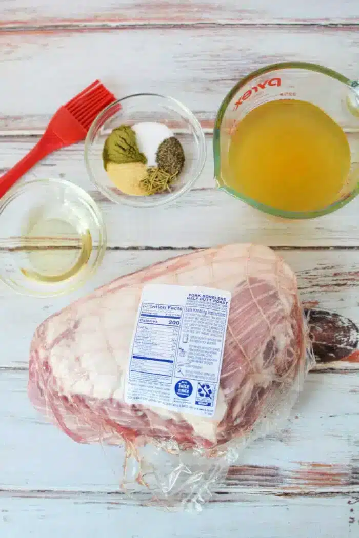 A raw pork shoulder roast in plastic packaging is placed on a wooden surface.