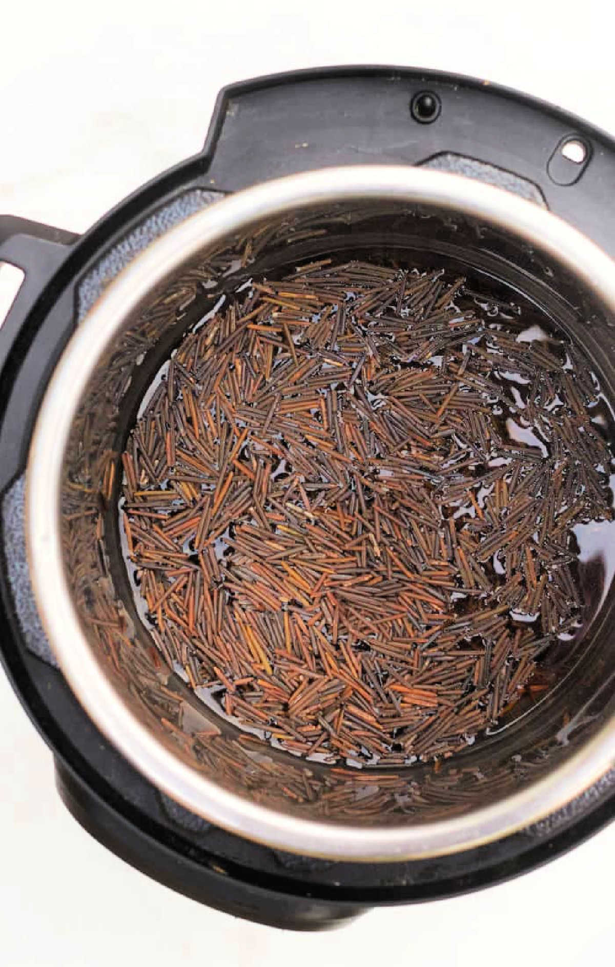 Uncooked wild and black rice soaking in water inside an Instant Pot, viewed from above.