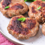 Sausage patties cooked to perfection, resting on a white plate with fresh greens in the background, bring an inviting aroma from the oven.