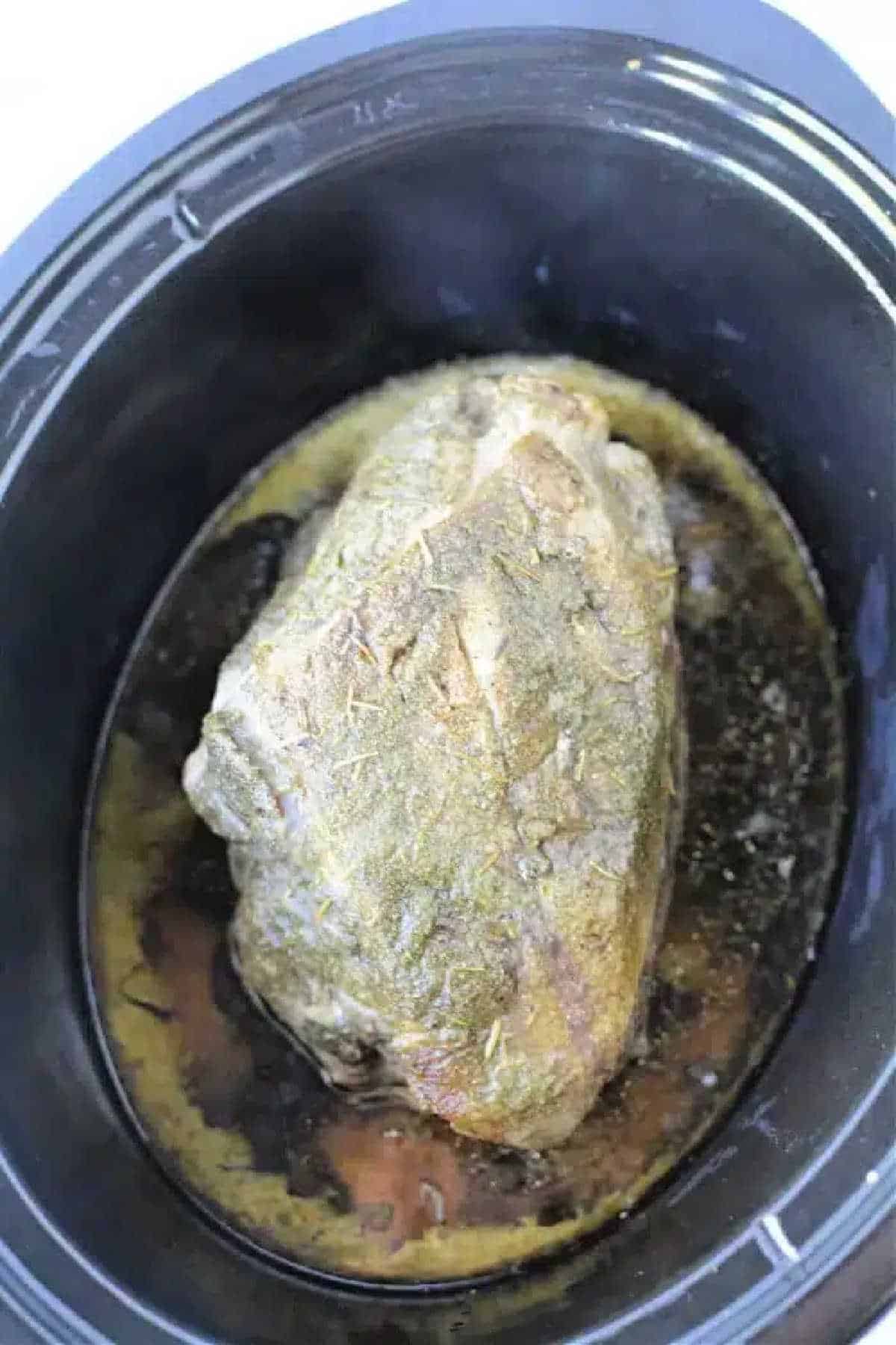 A seasoned 3 Ingredient Pork Roast simmers in a black slow cooker, with savory juices collecting at the bottom.