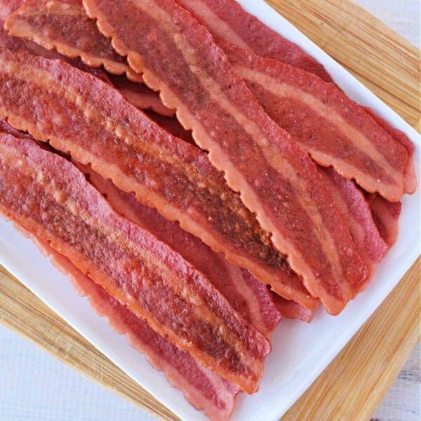 Slices of turkey bacon in the oven are arranged on a white tray atop a wooden board.