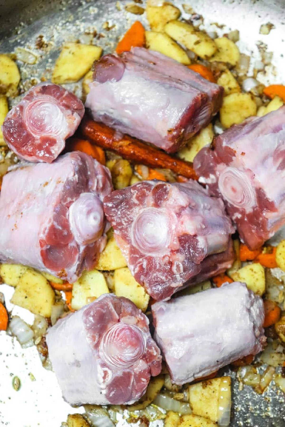 Raw oxtail pieces on top of chopped vegetables and spices in a metal pan, ready for cooking a flavorful Oxtail Pho.