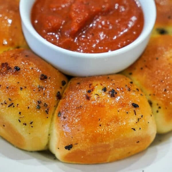 Golden baked Frozen Rolls in Air Fryer surround a bowl of marinara sauce on a white plate.