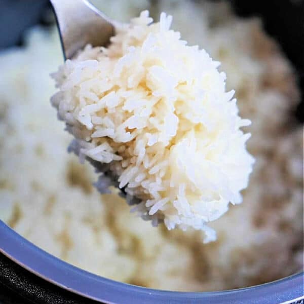 A spoonful of cooked jasmine rice is held over a pot, with a hand holding the spoon—perfectly fluffy from cooking jasmine rice in an Instant Pot.