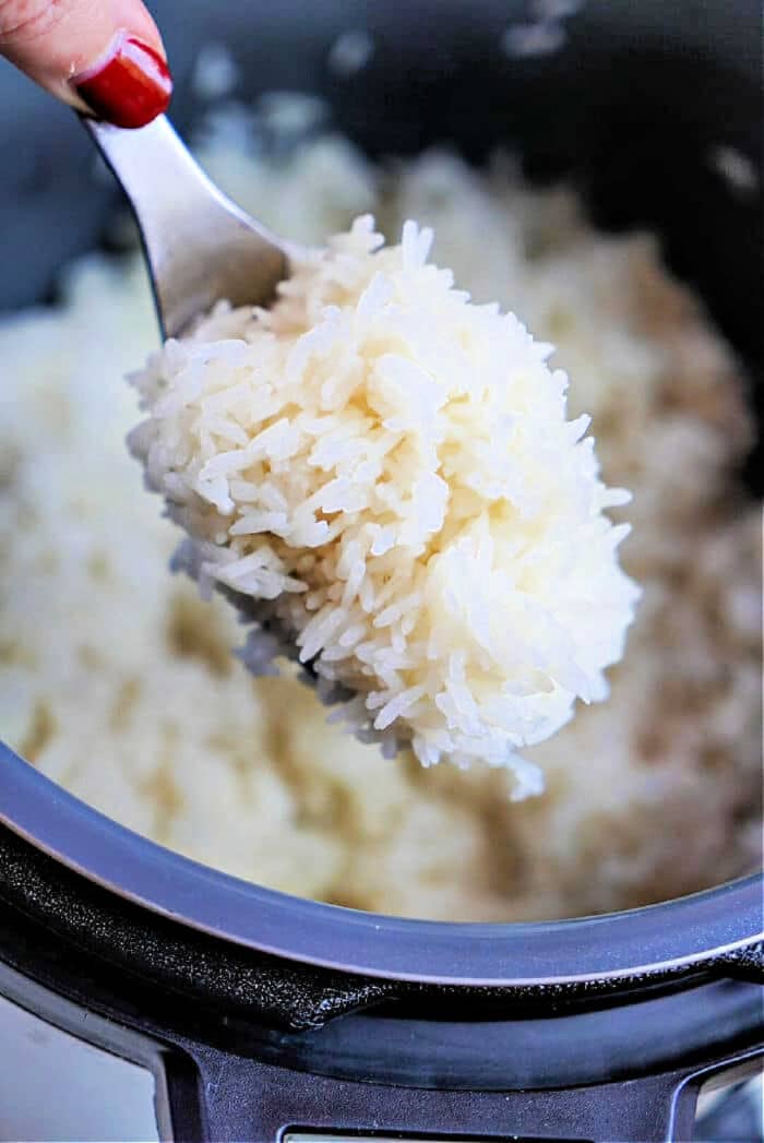 A spoonful of cooked jasmine rice is held over a pot, with a hand holding the spoon—perfectly fluffy from cooking jasmine rice in an Instant Pot.