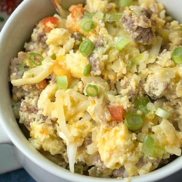 Bowl of scrambled eggs with sausage, cheese, potatoes, and chopped green onions, with a spoon—just like the comforting flavors you’d find in a classic crockpot breakfast casserole recipe.