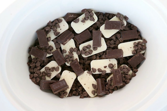 Chocolate chips, white candy melts, and chocolate pieces in a white bowl, ready to be melted for delicious crockpot peanut clusters.