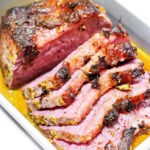 Sliced corned beef with a browned, seasoned crust in a metal tray with juices, perfect for serving alongside Dutch oven corned beef and cabbage.