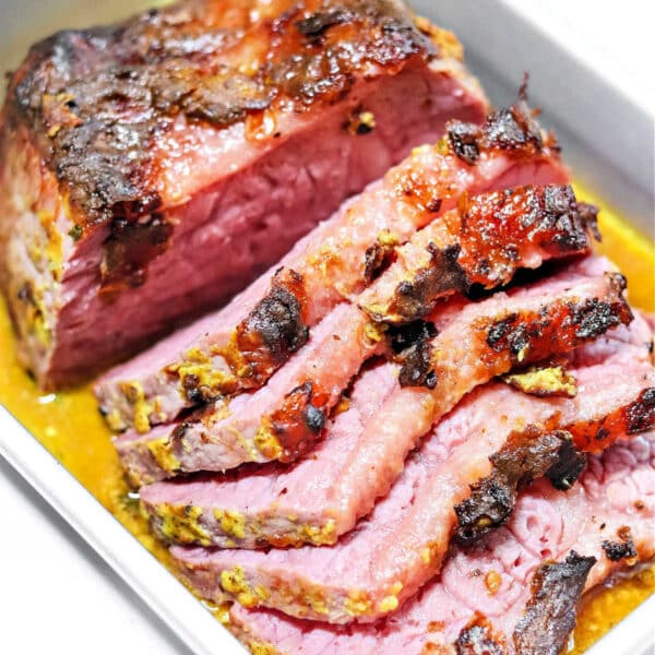 Sliced corned beef with a browned, seasoned crust in a metal tray with juices, perfect for serving alongside Dutch oven corned beef and cabbage.