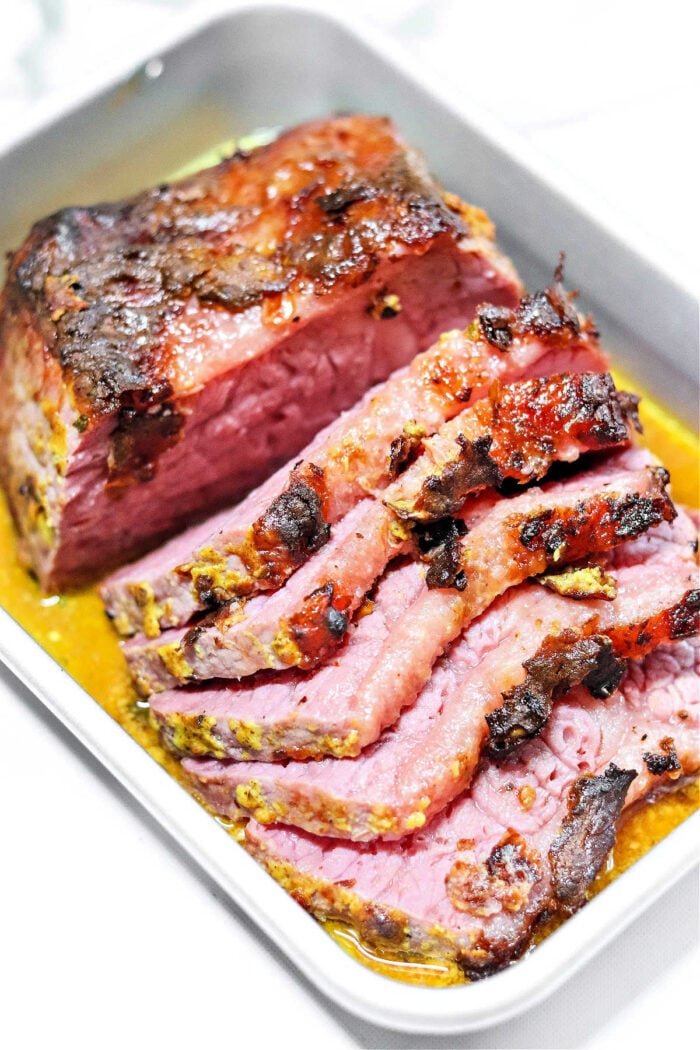 Sliced corned beef with a browned, seasoned crust in a metal tray with juices, perfect for serving alongside Dutch oven corned beef and cabbage.