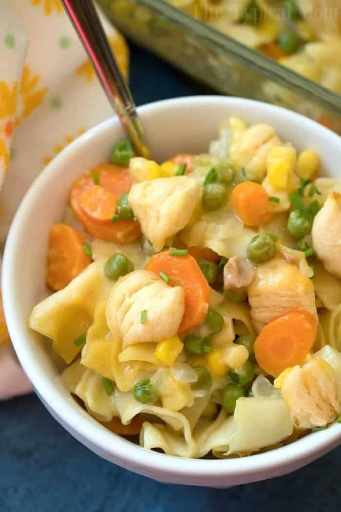 Chicken pot pie casserole my whole family loves! Total comfort food made casserole style loaded with chicken and vegetables with a retro style crust. #chicken #potpie #casserole #chickenpotpie Bowl of creamy easy chicken pot pie casserole with carrots, peas, and corn, served with a fork in the bowl.
