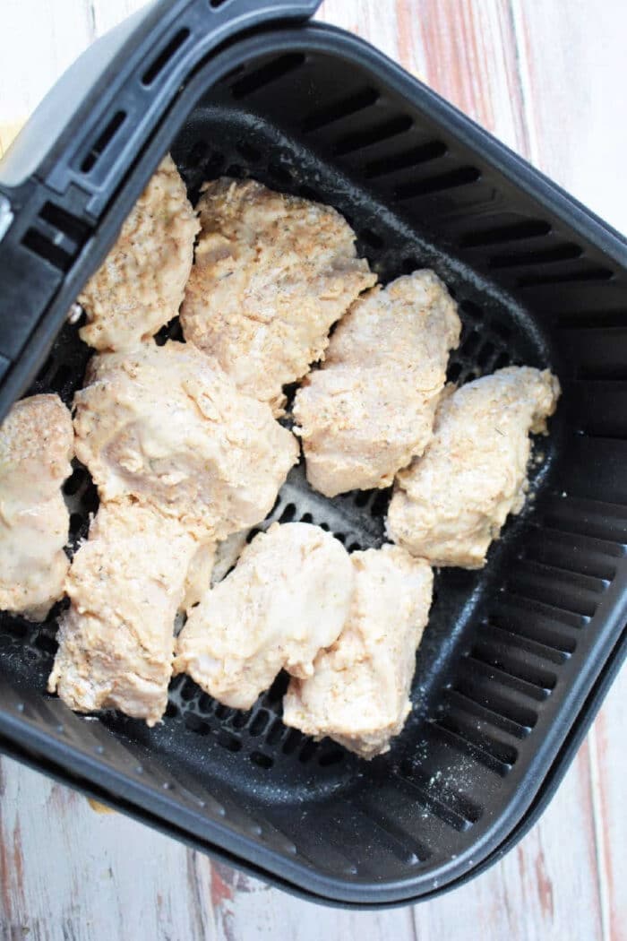 Raw, breaded air fryer fried chicken breast pieces arranged inside an air fryer basket on a wooden surface.