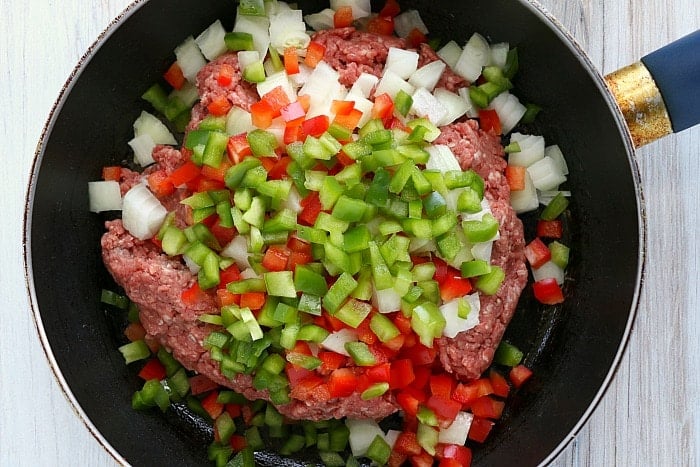 Ground meat with chopped onions, red and green bell peppers sizzles in a black frying pan, perfect for stuffing into air fryer empanadas.