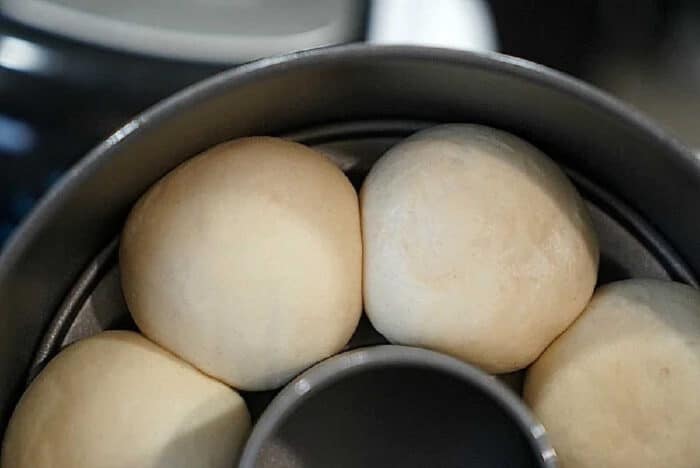 Four round dough balls, perfect for making frozen rolls in air fryer, are arranged in a circular metal baking pan, ready to be baked.