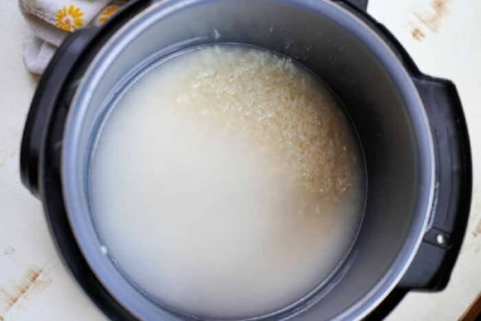 Uncooked rice soaking in cloudy water inside a black pot, seen from above—an essential first step when cooking jasmine rice in an Instant Pot.