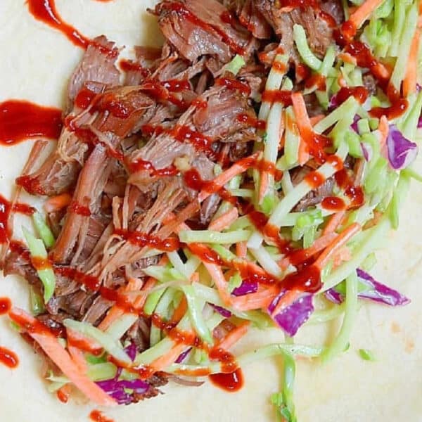 Slow cooker Korean beef, slaw, and red sauce on a tortilla, ready to be wrapped.