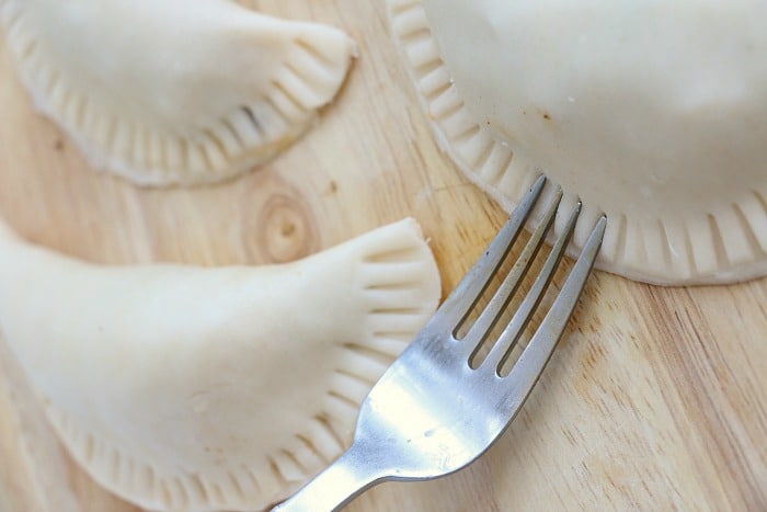 Three uncooked air fryer empanadas rest on a wooden surface, with one showing the delicate marks of a fork pressing its edges.